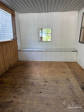 Empty unfinished room with wood floor, white paneled walls, and a small window.