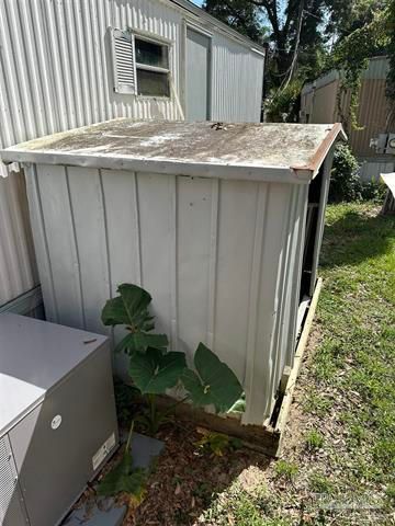 Weathered white shed beside a mobile home, with a rusted roof and large green leaves at the base.