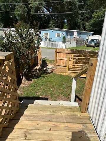 Wooden steps leading to a fenced backyard with grass, trees, and a blue mobile home in the background