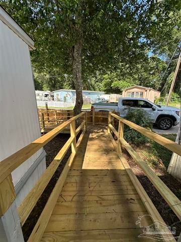 Wooden wheelchair ramp beside a white building, with railings, trees, and parked vehicles nearby.