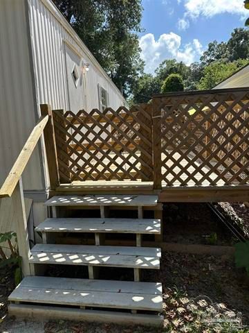 Outdoor wooden stairs beside a house, leading to a lattice-railed deck on a sunny hillside