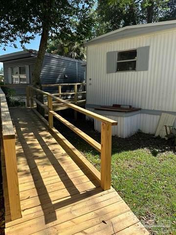 Wooden accessibility ramp with railings leading to a white mobile home in a grassy yard