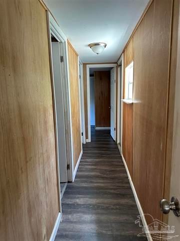 Narrow hallway with wood-paneled walls, dark flooring, white trim, and a window on the right.