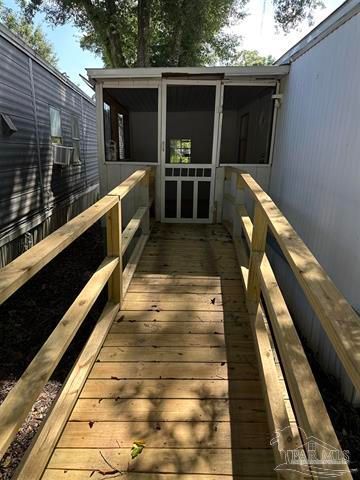 Wooden ramp leading to a small screened porch between two buildings, with sunlight and shadows.