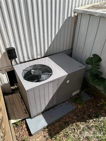 Outdoor air conditioning unit beside a corrugated wall, with leaves nearby.