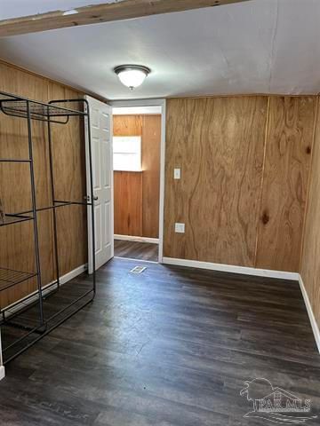 Empty room with dark wood floor, plywood walls, open closet rack, and a door to a small windowed space.