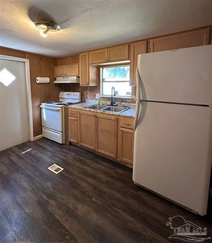 Small kitchen with white appliances, wood cabinets, dark floor, and a window over the sink.