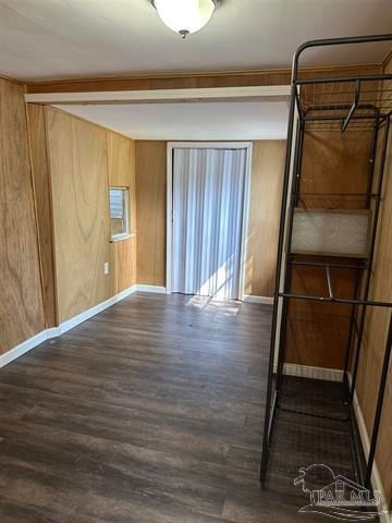 Empty room with wood-paneled walls, dark flooring, sliding door, and metal shelving unit at right.
