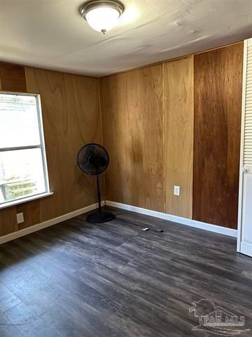Empty room with wood-paneled walls, dark floor, a window, and a black standing fan.