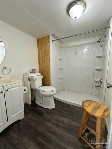 Bright bathroom with white vanity, toilet, walk-in shower, wood stool, and dark wood floor