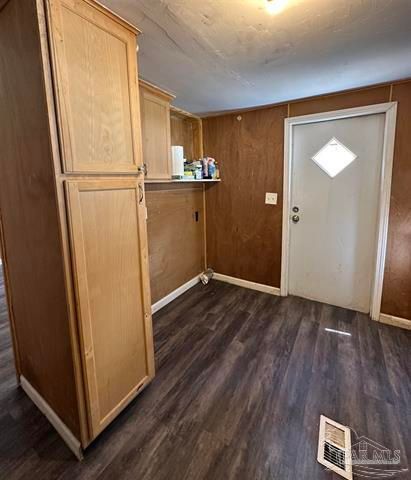Small wood-paneled room with cabinet, shelf, white door, and dark wood flooring.