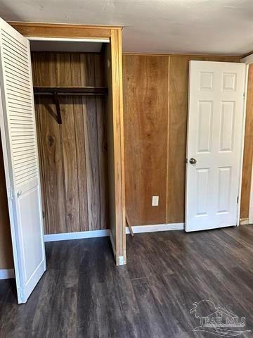 Empty bedroom with open closet, wood-paneled walls, gray floor, and two white doors