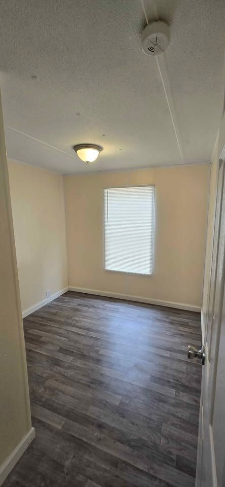 Empty small room with wood flooring, beige walls, a ceiling light, and a window with blinds.