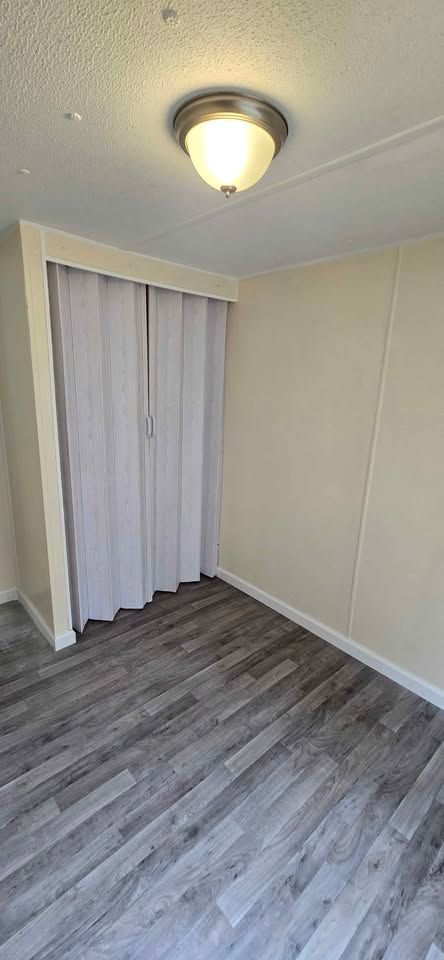 Small empty room with gray wood flooring, white walls, and a closet with white curtains.
