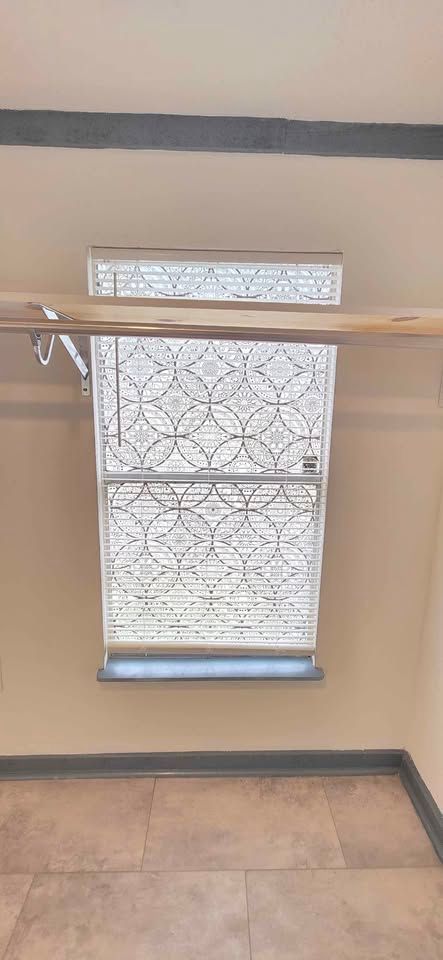 Decorative window with patterned shade above a wooden railing in a tiled indoor hallway