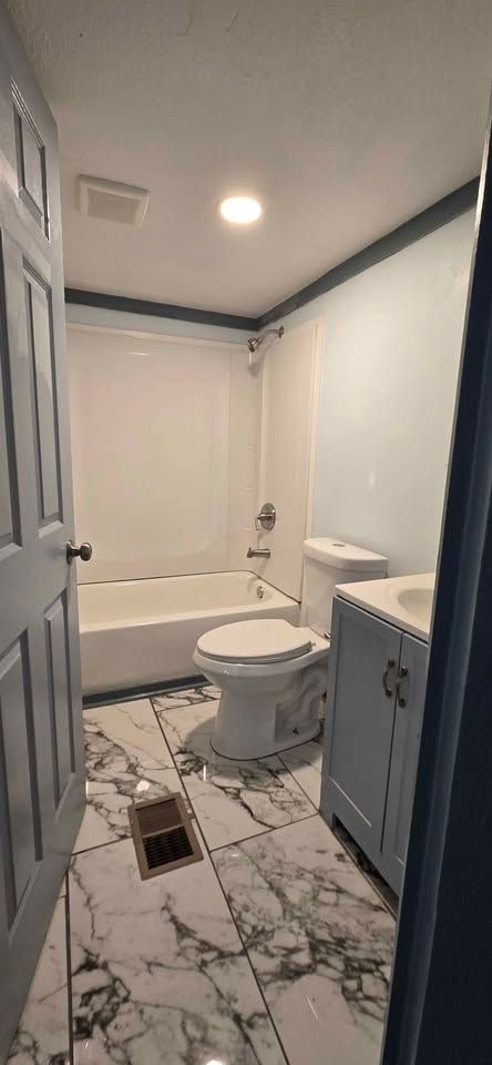 Small white bathroom with tub, toilet, vanity, and marble-look tile floor
