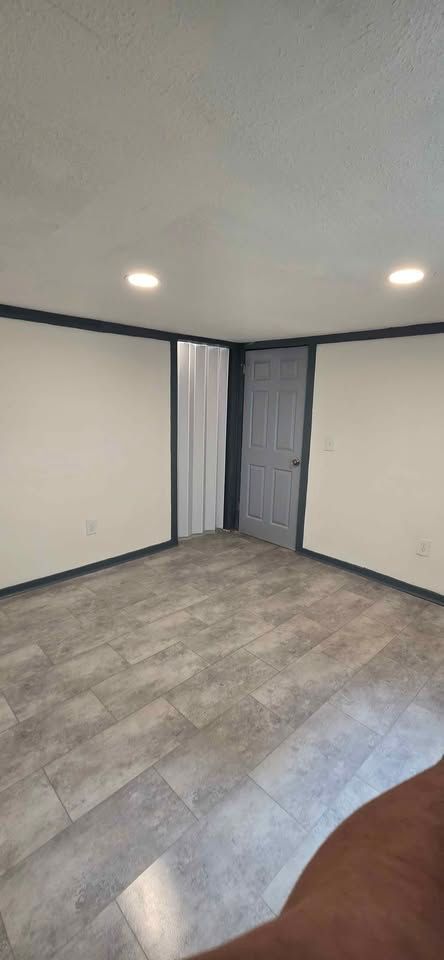 Empty room with gray tile floor, beige walls, recessed lights, and a doorway with curtains.