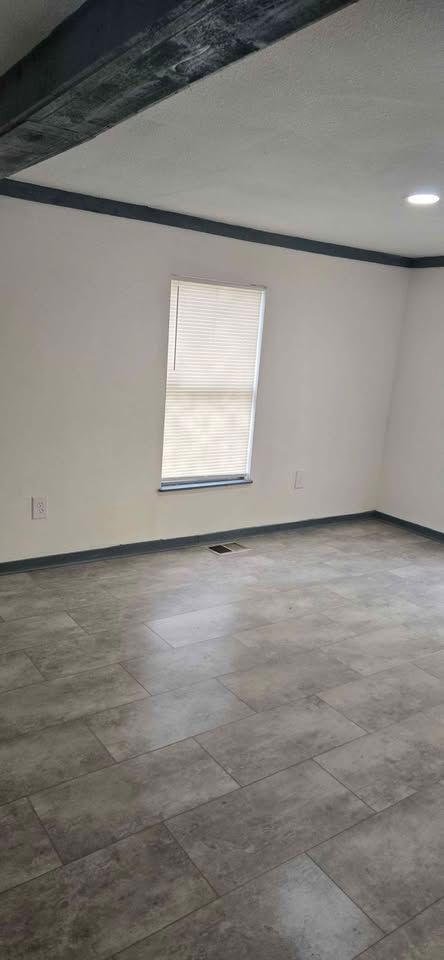 Empty unfurnished room with gray tile floor, white walls, and a single window with a blind.