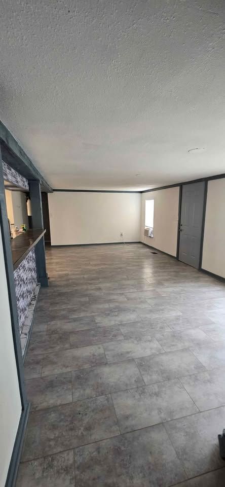 Empty living room with gray tile floor, white walls, and a large front window.