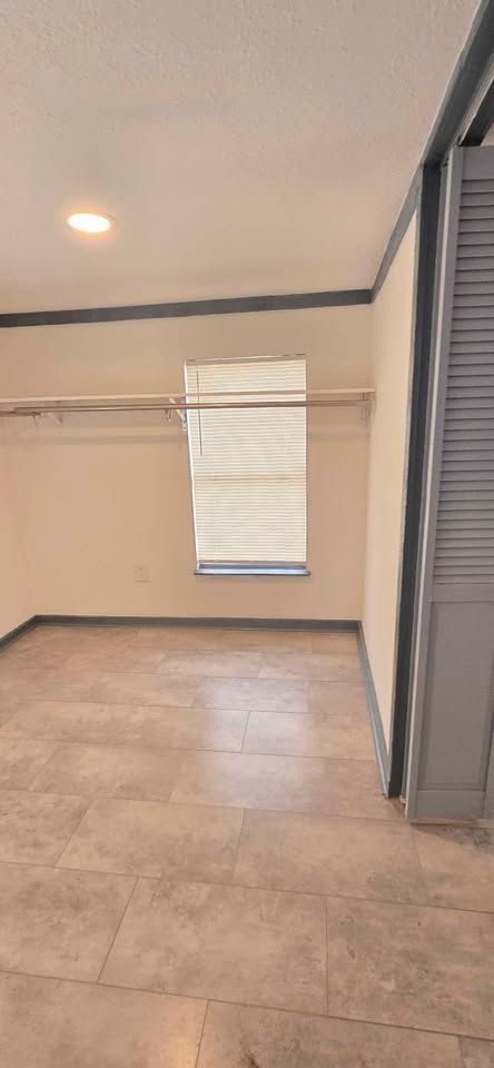 Empty tiled room with beige walls, a window with blinds, and a sliding glass door