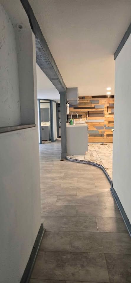 Narrow hallway with gray walls and wood floor leading into a bright modern living space