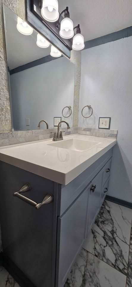 Modern bathroom vanity with white sink, lit mirror, dark cabinets, and marble-style tile floor