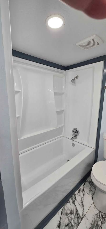 Small white bathroom with a bathtub, shower fixtures, toilet, and ceiling light.