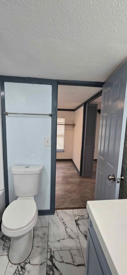 Small bathroom with toilet, shower partition, marble-look floor, and a doorway to a hall.