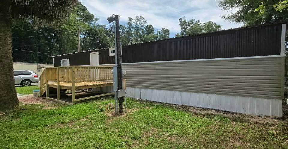 Wooden ramp beside a corrugated metal fence in a grassy yard under trees