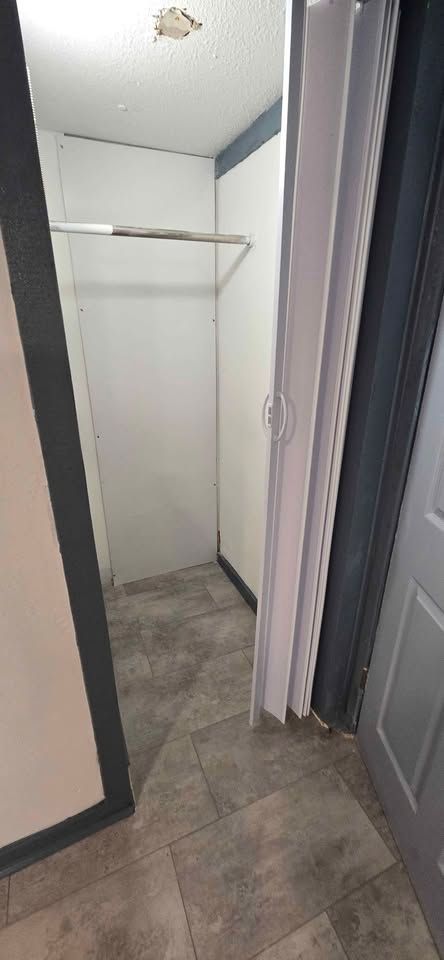 Narrow hallway view into a small empty closet with white walls, a shelf, and gray carpet.