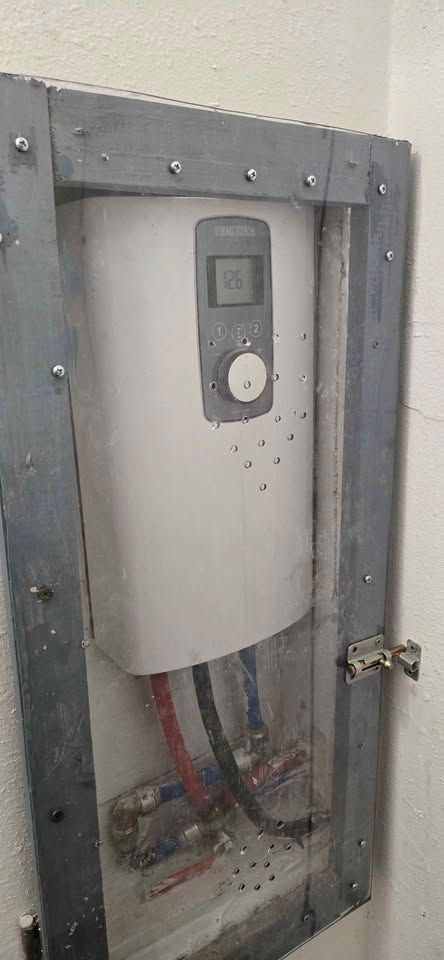 Open electrical panel with exposed wires and gray breaker box mounted in wall.