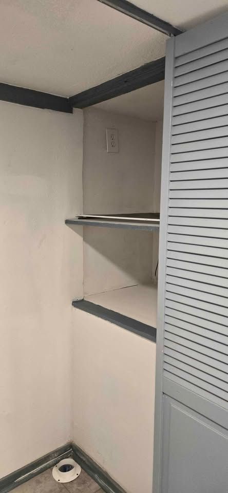 Open closet with shelves, hanging rod, louvered door, and a pet dish on the floor.