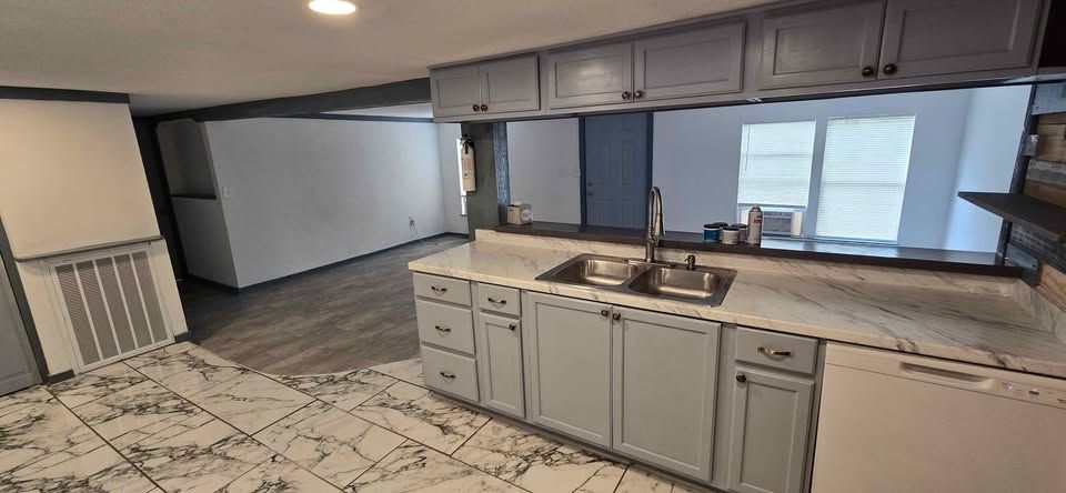 Empty kitchen and living area with gray cabinets, tiled floor, and large windows.
