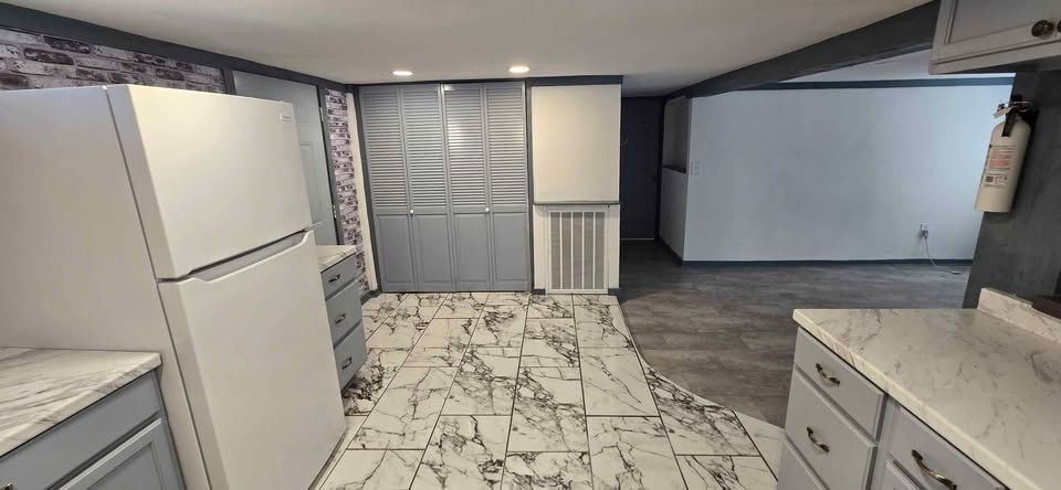 Modern kitchen with white cabinets, marble tile floor, and a view into a carpeted living area