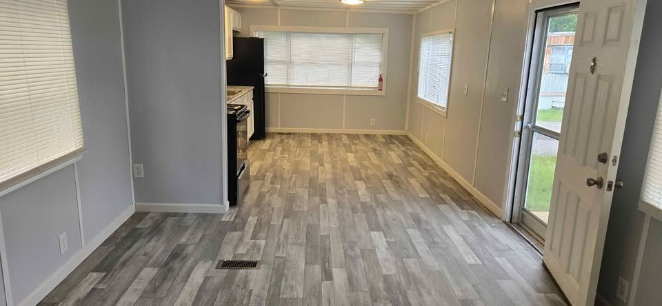 Empty gray living room with wood-look flooring, windows, and a glass front door