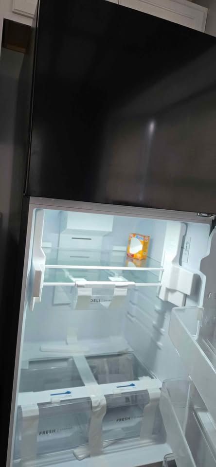 Open refrigerator with empty white shelves and a bright interior light.