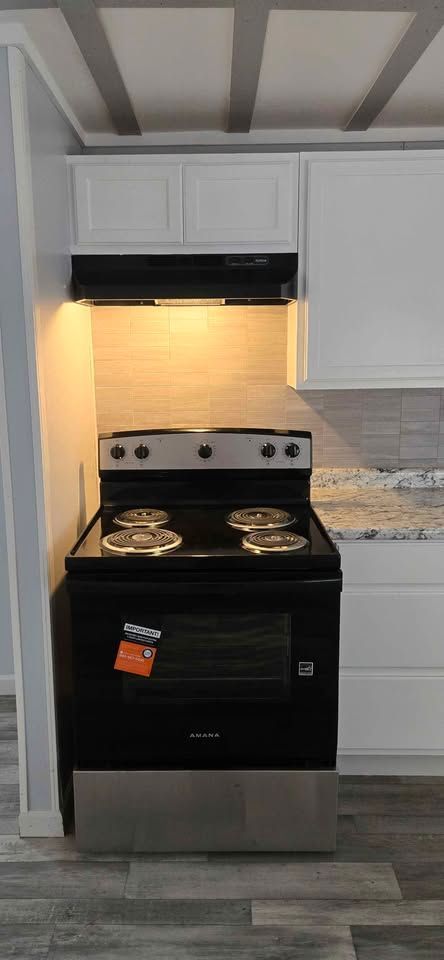 Black gas stove centered in a bright kitchen with white cabinets and hood