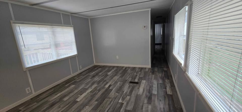 Empty gray room with wood-look flooring and large windows with blinds