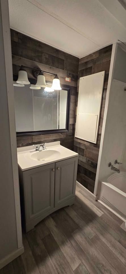 Small bathroom with vanity, mirror, lights, wood-look floor, and shower/tub on the right.