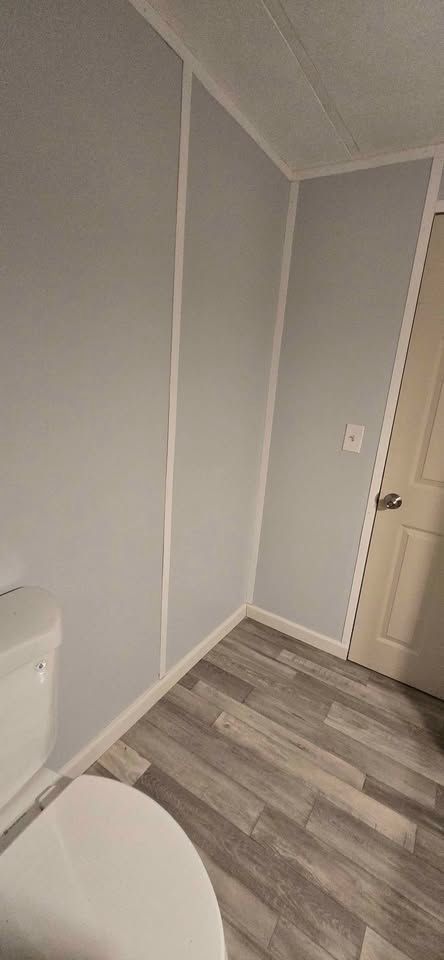 Small bathroom corner with gray walls, wood-look floor, toilet edge, and a closed white door
