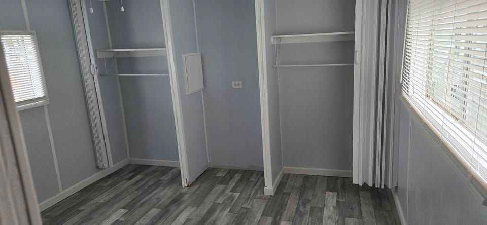Empty gray closet with open shelves, hanging rods, and carpeted floor beside a window