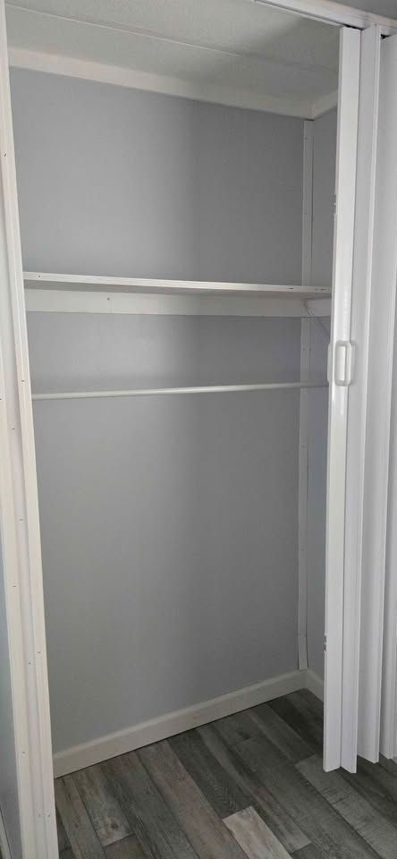 Empty gray closet with white shelves, hanging rod, and wood-patterned floor.