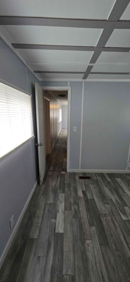 Narrow hallway with gray walls, wood-look flooring, and a doorway leading to another room.
