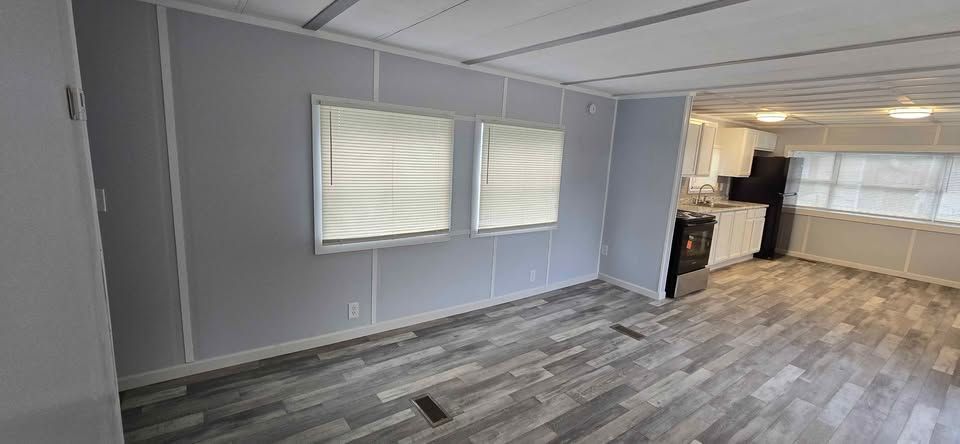 Empty living room with gray walls, wood-look flooring, and kitchen area in the back