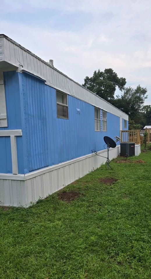 Blue mobile home with white trim beside a grassy yard under a cloudy sky