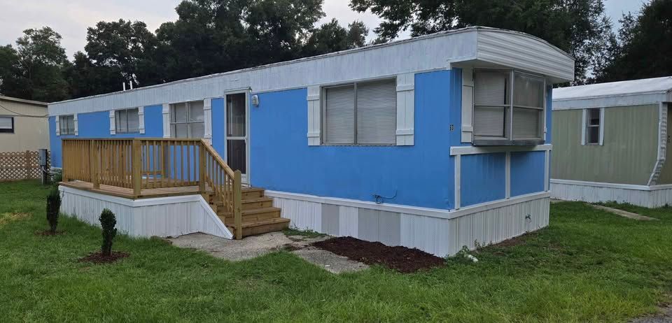 Blue mobile home with a small wooden porch and stairs on a grassy lot
