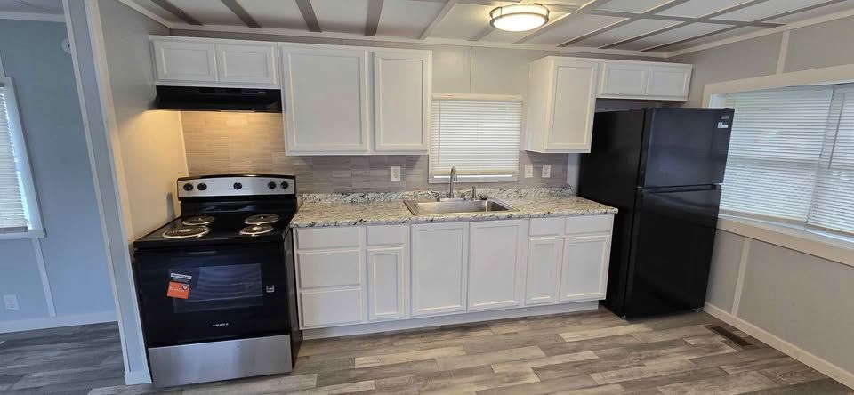 Small kitchen with white cabinets, black appliances, gray floor, and window over the sink.