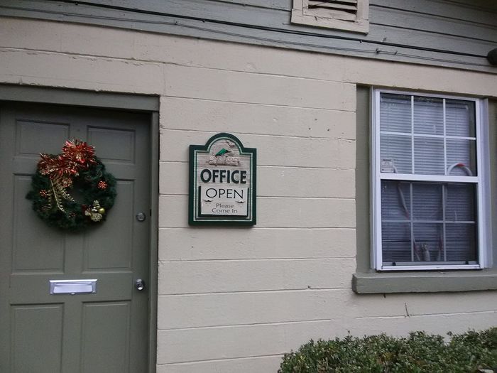 Office entrance with green door, wreath, and “Open” sign beside a window.