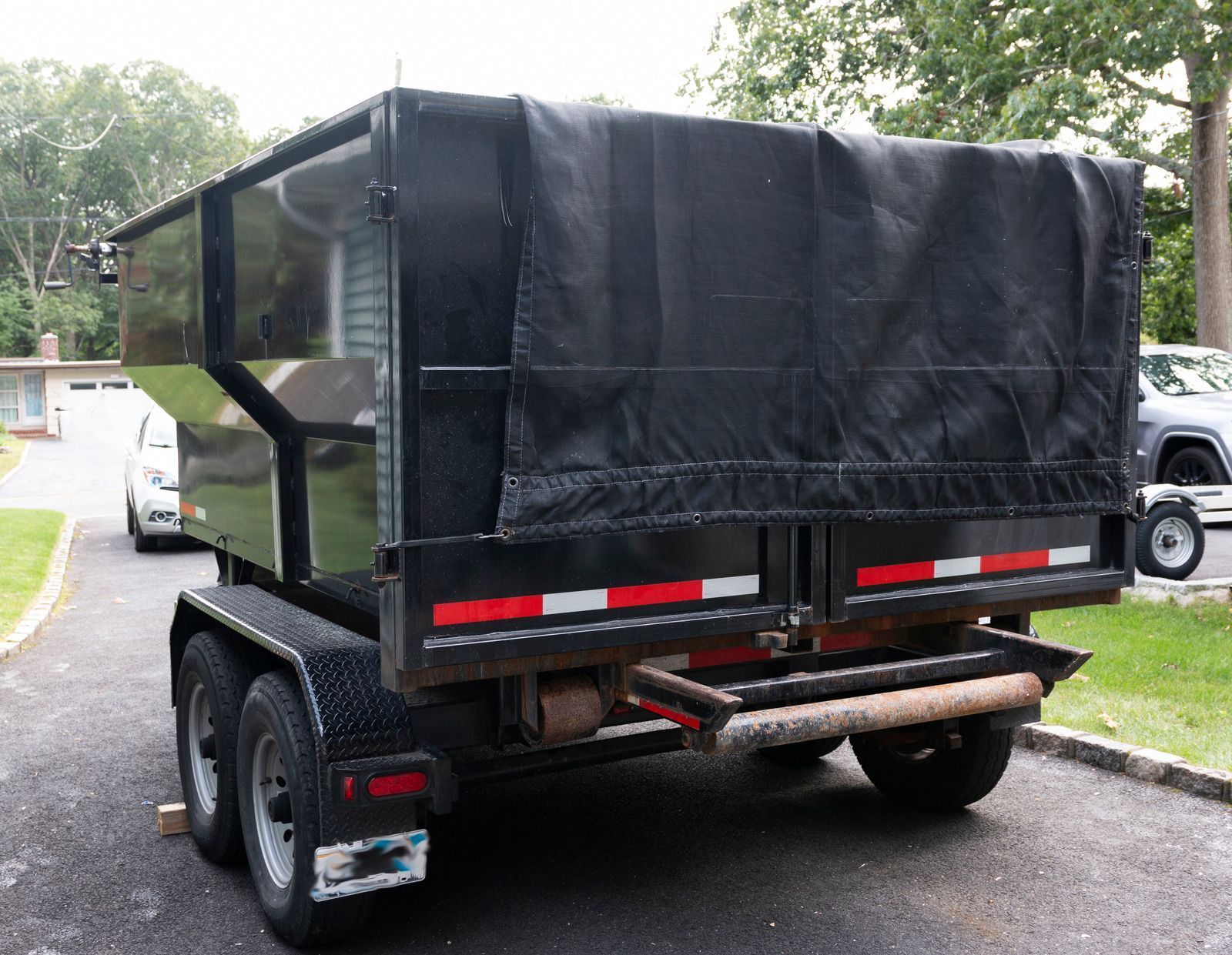 Black dumpster trailer with a tarp cover, parked on asphalt.