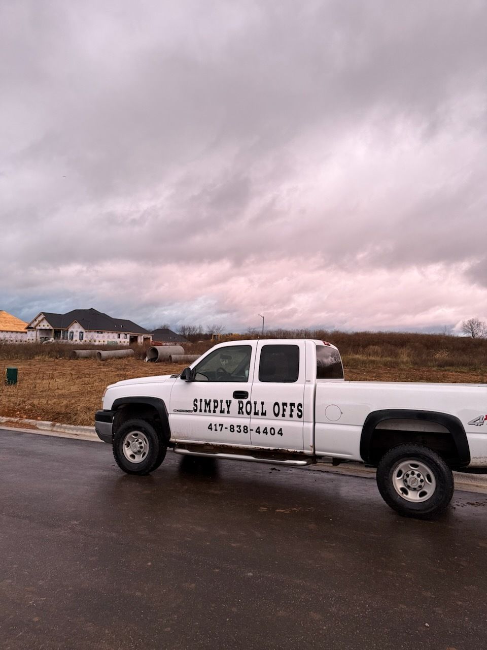 White pickup truck with company lettering parked on a wet road under a cloudy sky